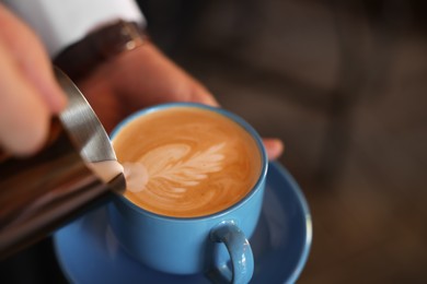 Photo of Barista pouring milk into cup of coffee on blurred background, closeup. Space for text