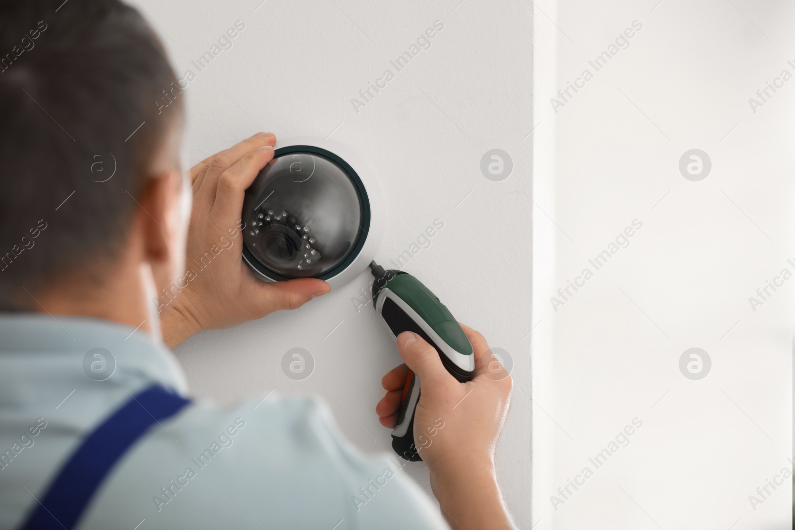 Photo of Technician installing CCTV camera on wall indoors, closeup