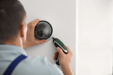 Technician installing CCTV camera on wall indoors, closeup