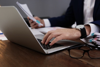 Photo of Businessman working with laptop and documents at table, closeup