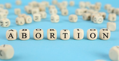 Photo of Word Abortion made of wooden cubes on light blue background, closeup