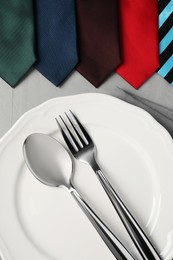 Photo of Business lunch concept. Plate, cutlery and ties on light gray table, flat lay