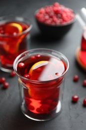 Photo of Tasty hot cranberry tea with lemon and fresh berries in glass on black textured table