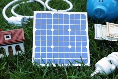 Photo of Composition with solar panel, house model and lightbulb on green grass