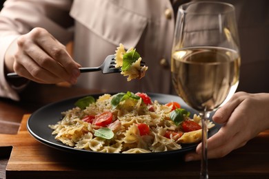 Photo of Woman eating delicious pasta with tomatoes and basil at wooden table, closeup