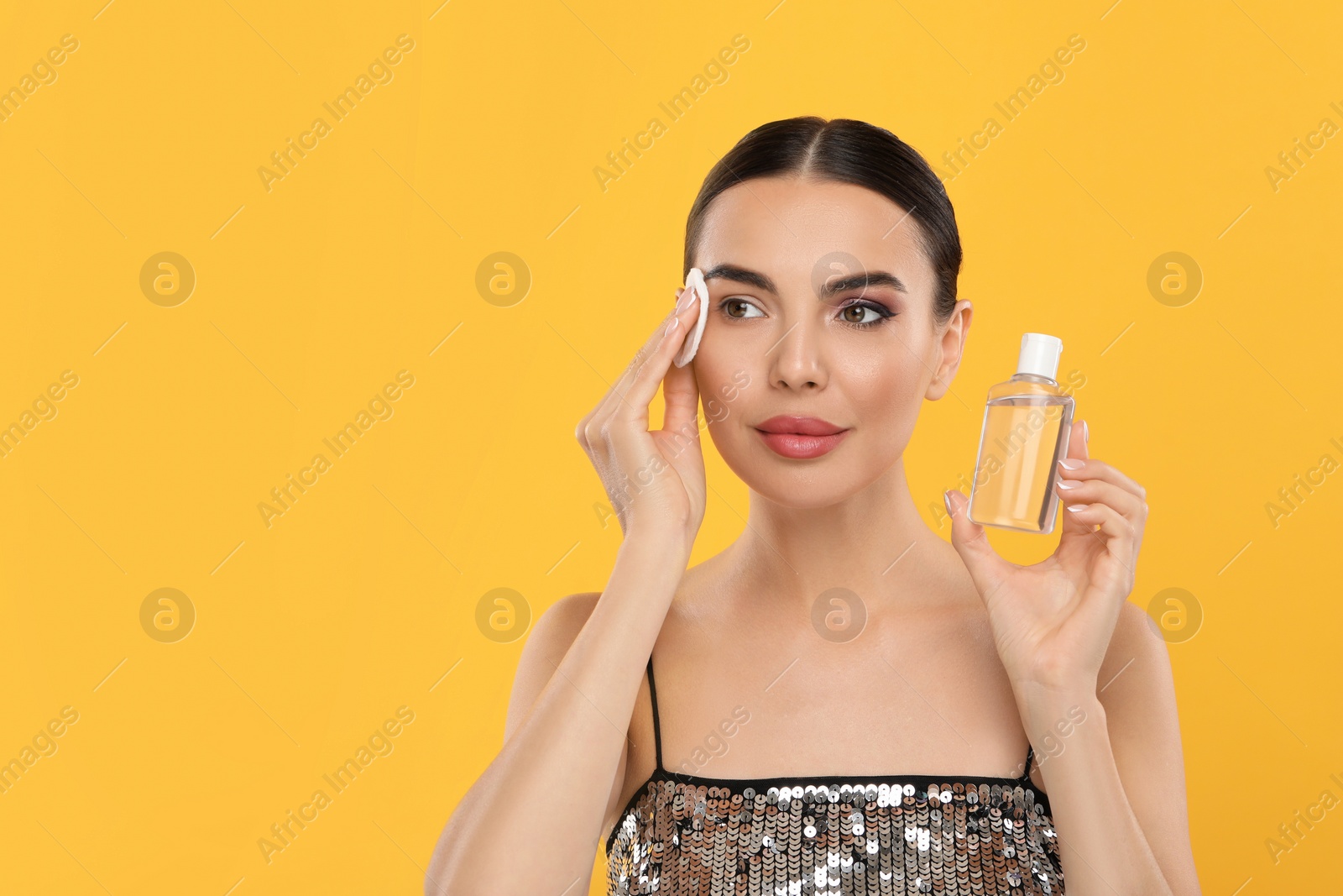 Photo of Beautiful woman removing makeup with cotton pad on orange background, space for text