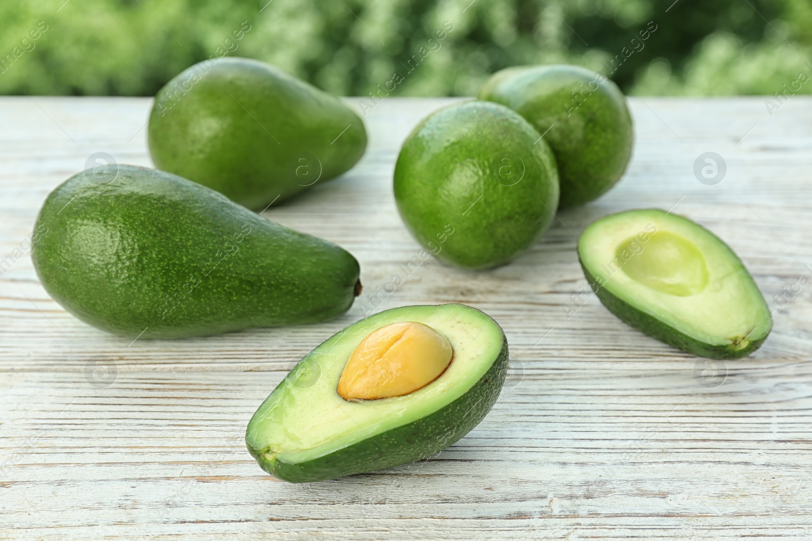 Photo of Ripe avocados on wooden table against blurred background