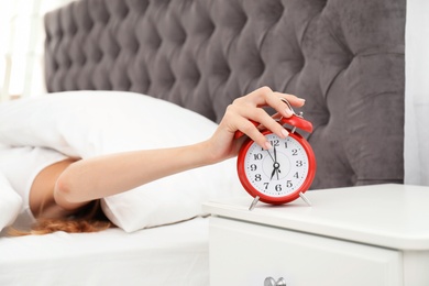 Woman turning off alarm clock in bedroom