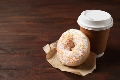 Yummy donut and paper cup on wooden table, space for text