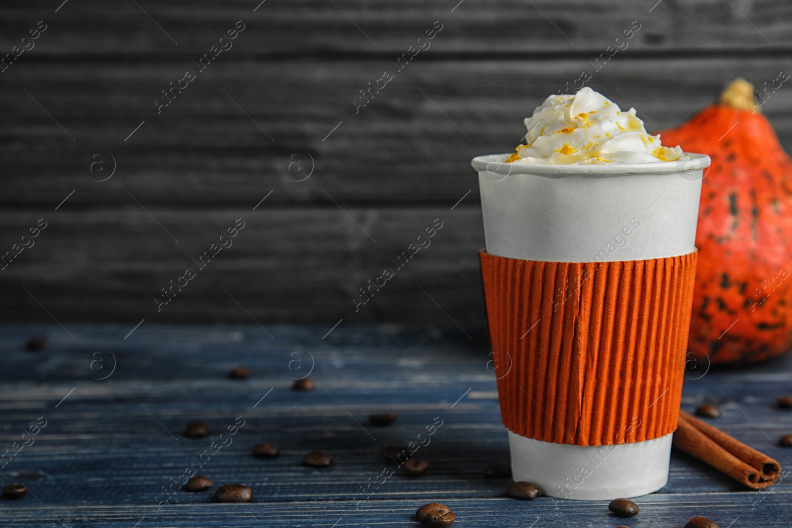 Photo of Takeaway paper cup with pumpkin spice latte and whipped cream on wooden table. Space for text