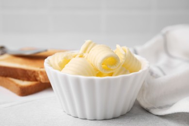 Tasty butter curls in bowl and toasts on light grey table, closeup