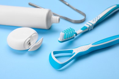 Photo of Tongue cleaners and other oral care products on light blue background, closeup