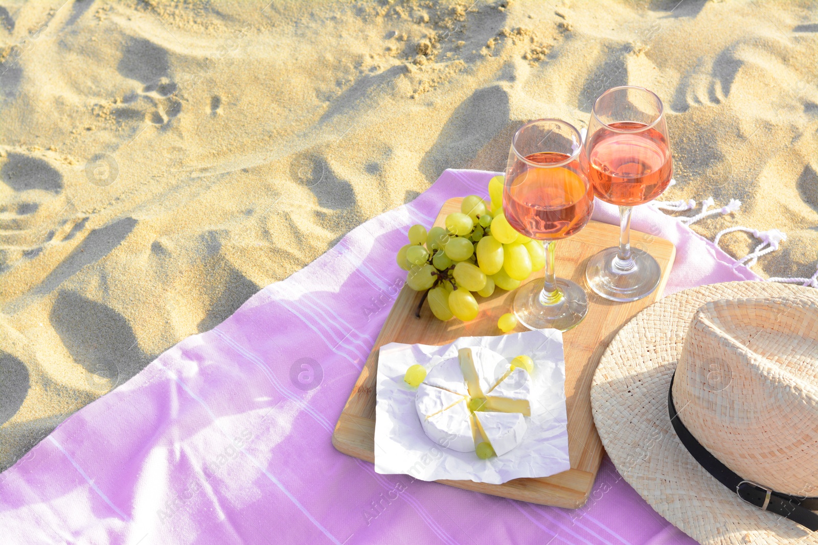 Photo of Glasses with rose wine and snacks on beach sand outdoors. Space for text