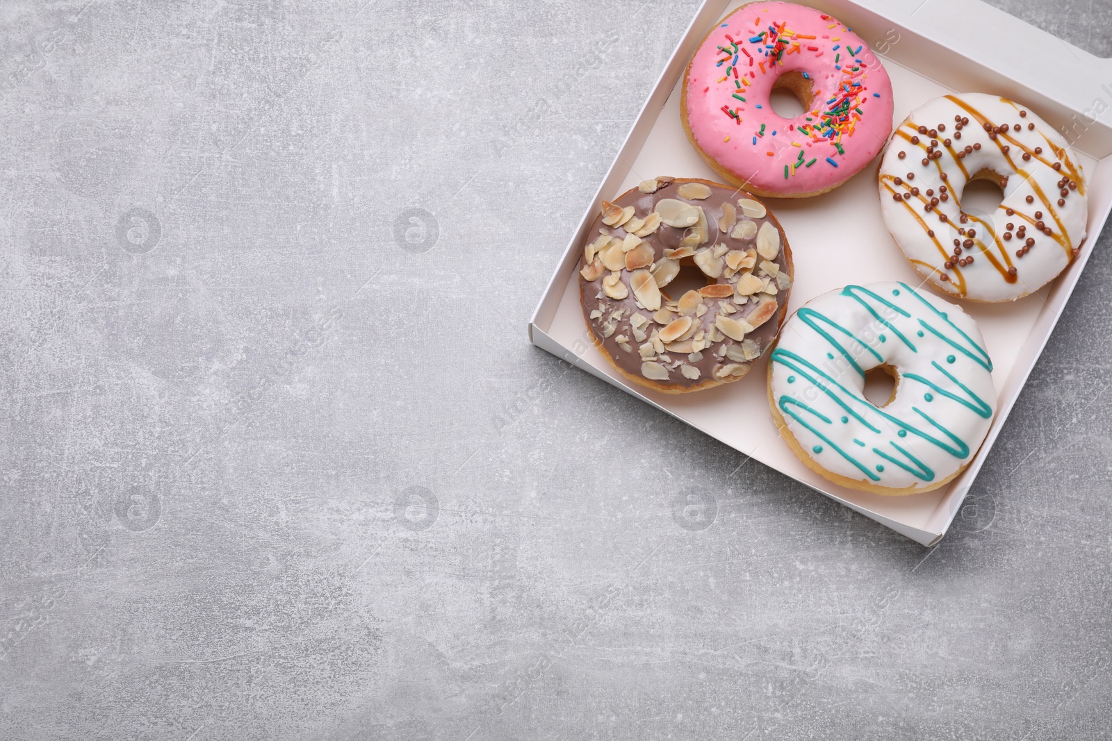 Photo of Box with different tasty glazed donuts on light grey table, top view. Space for text