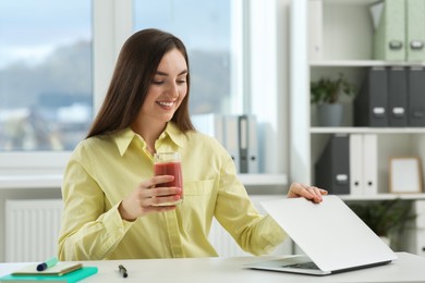 Photo of Beautiful young woman with delicious smoothie at workplace in office