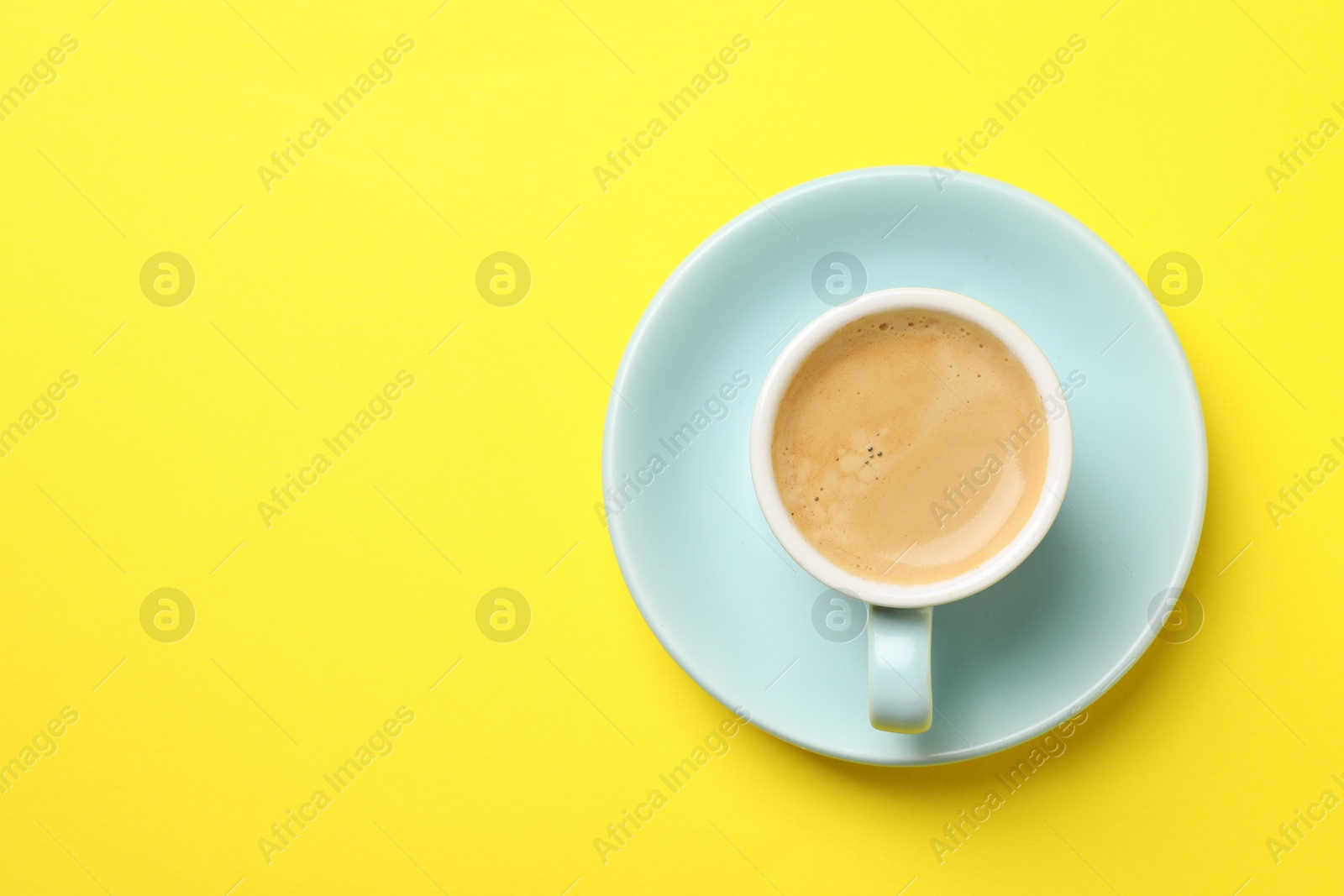 Photo of Aromatic coffee in cup on yellow background, top view. Space for text