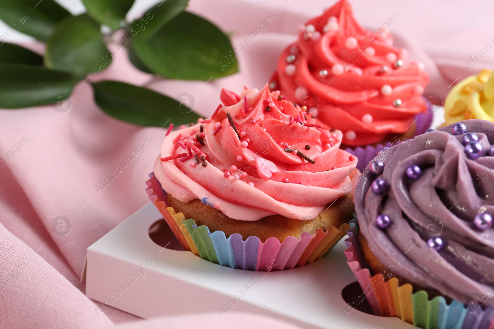 Photo of Delicious cupcake with bright cream on pink fabric, closeup