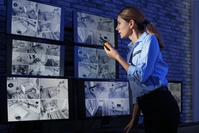 Female security guard with portable transmitter monitoring modern CCTV cameras indoors