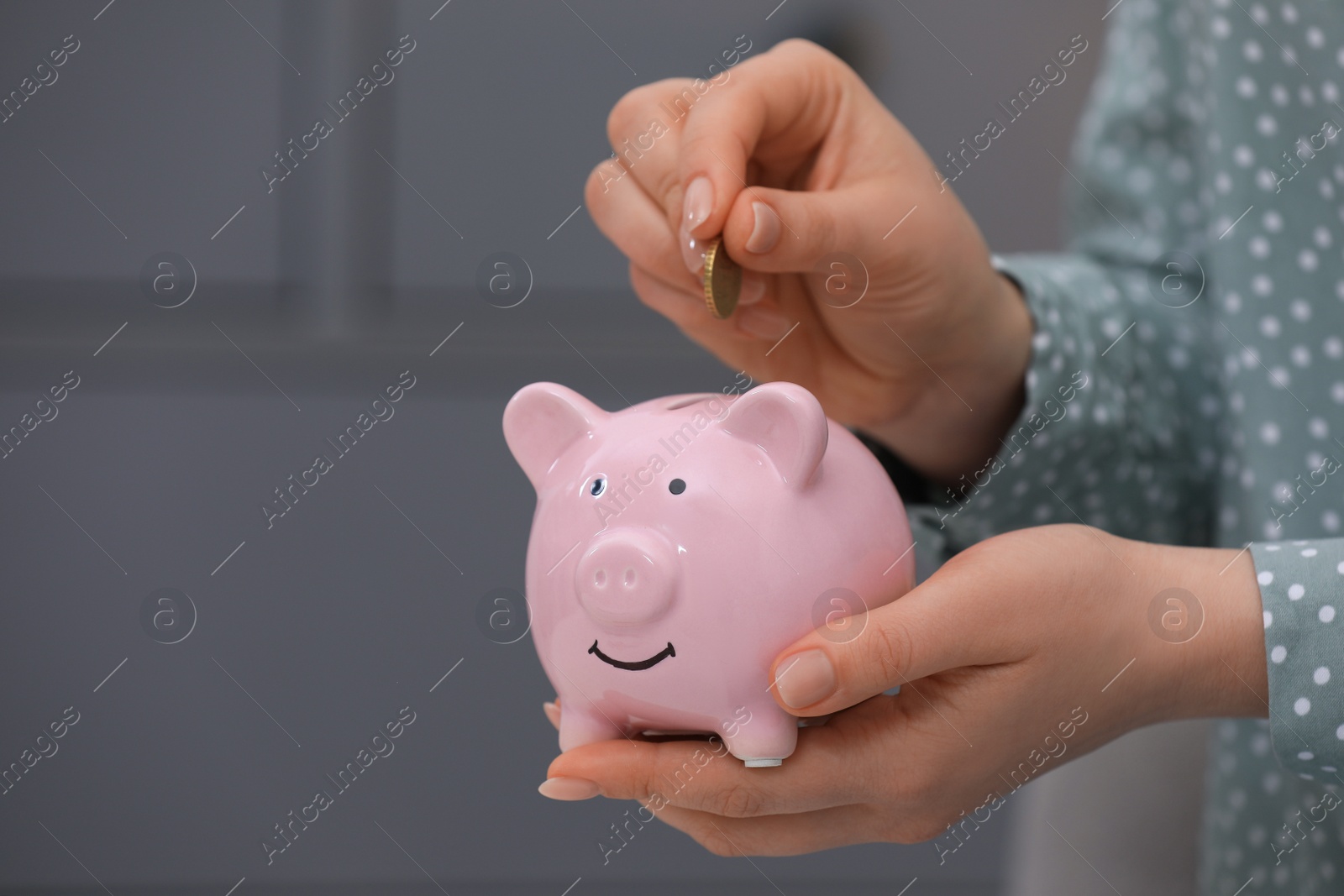 Photo of Young woman putting coin into piggy bank indoors, closeup