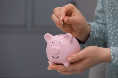 Young woman putting coin into piggy bank indoors, closeup