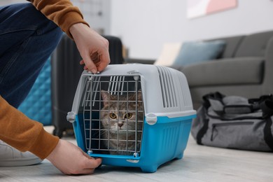 Photo of Travel with pet. Man closing carrier with cat at home, closeup