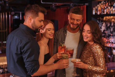 Photo of Happy friends clinking glasses with fresh cocktails in bar