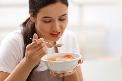 Photo of Young woman eating tasty vegetable soup indoors