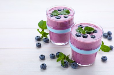 Photo of Glasses of blueberry smoothie with mint and fresh berries on white wooden table, space for text