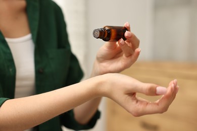 Aromatherapy. Woman with bottle of essential oil against blurred background, closeup