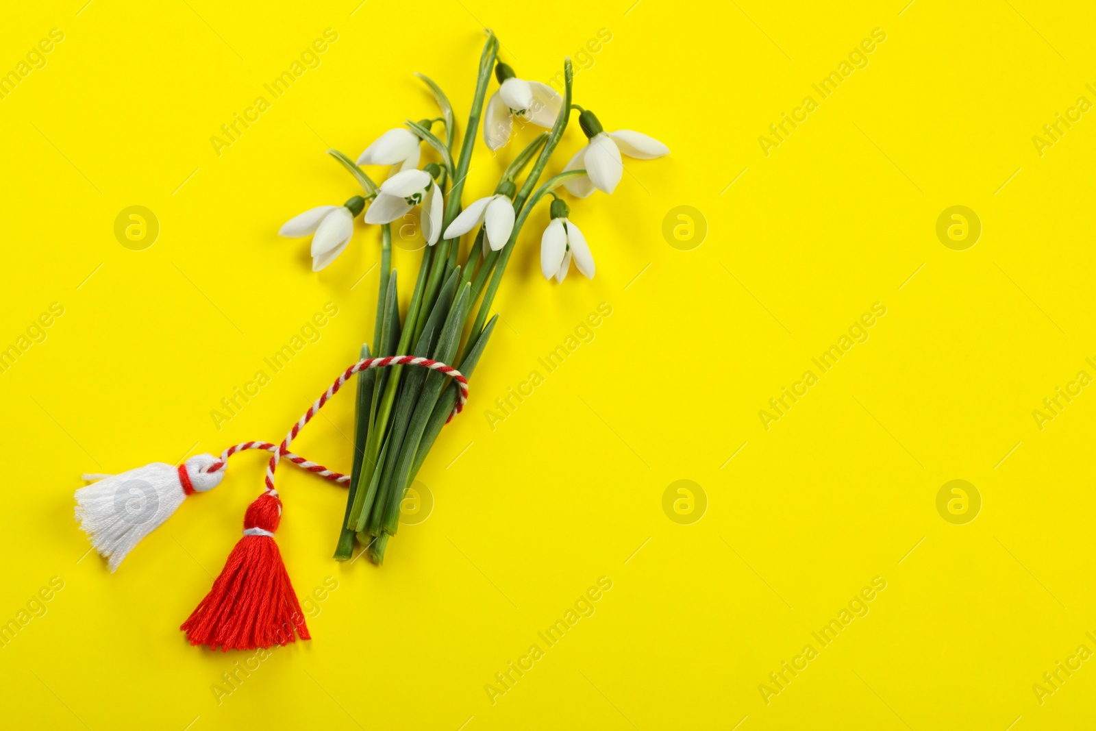Photo of Beautiful snowdrops with traditional martisor on yellow background, flat lay and space for text. Symbol of first spring day