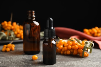 Photo of Ripe sea buckthorn and bottles of essential oil on grey table against black background