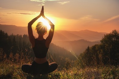 Woman practicing yoga in mountains at sunrise, back view