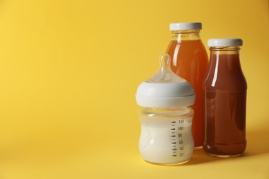 Photo of Bottles with milk and juice on yellow background, space for text. Baby nutrition