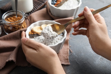 Photo of Young woman eating tasty chia seed pudding with banana and granola at table, closeup