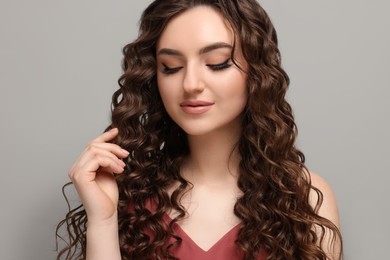 Photo of Beautiful young woman with long curly brown hair on grey background
