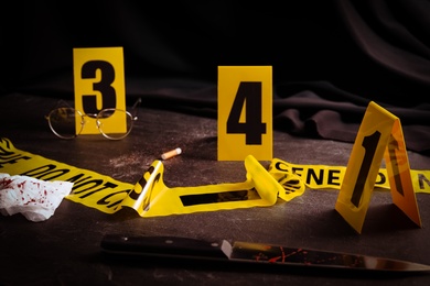 Photo of Bloody knife, tape and markers on black slate table. Crime scene