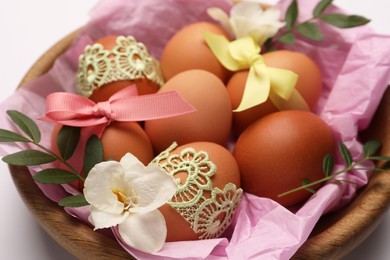 Photo of Easter eggs with colorful bows, twigs and flowers in bowl on white background, closeup