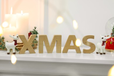 Word Xmas made of wooden letters and Christmas decor on white mantelpiece indoors