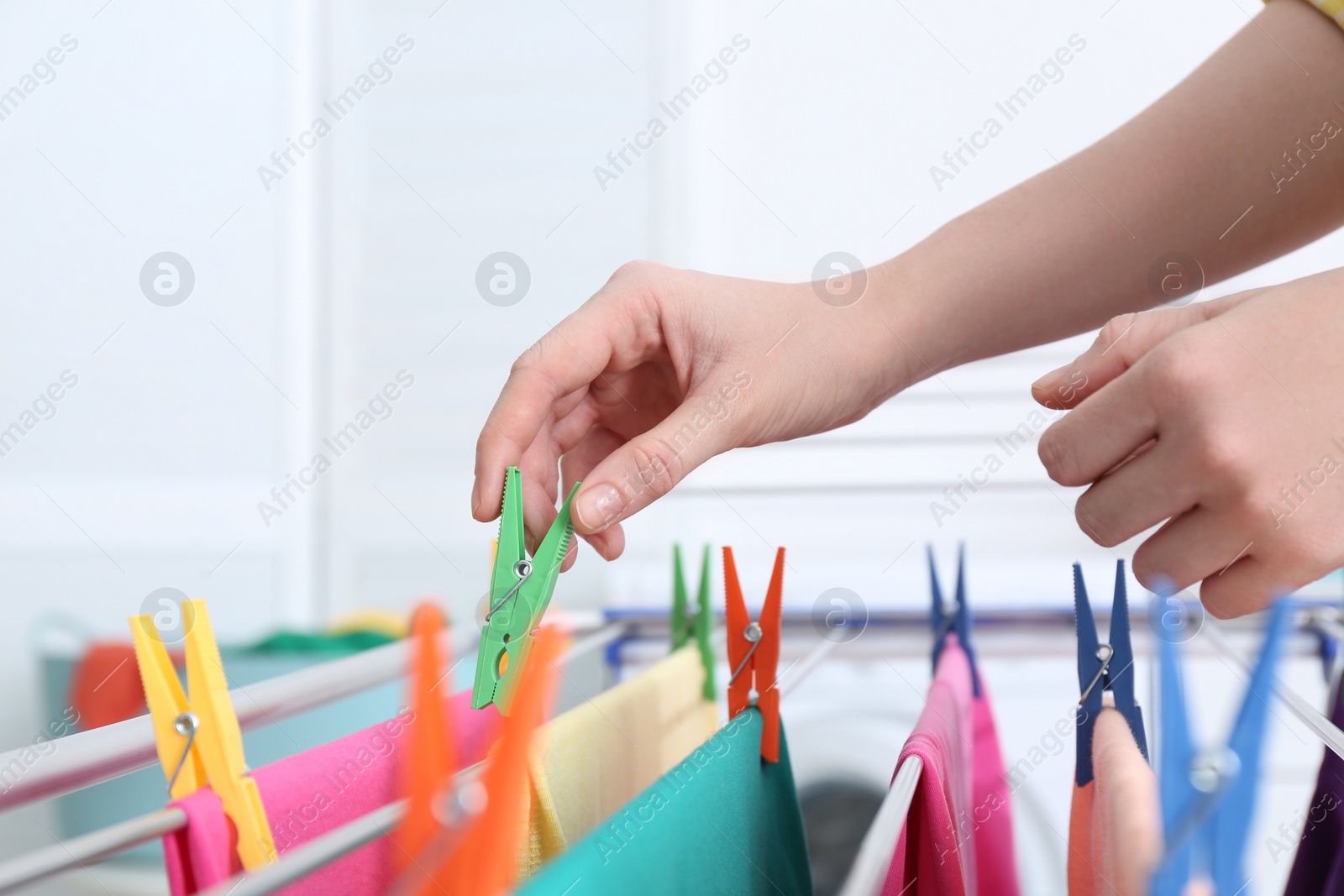 Photo of Woman hanging clean laundry on drying rack indoors, closeup