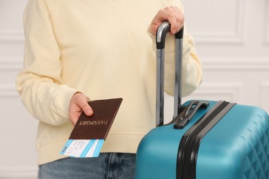 Photo of Tourist with suitcase giving passport and tickets on blurred background, closeup