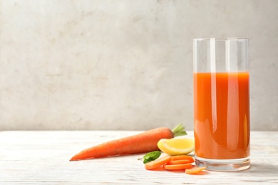 Glass of fresh carrot juice and ingredients on white wooden table against light background, space for text