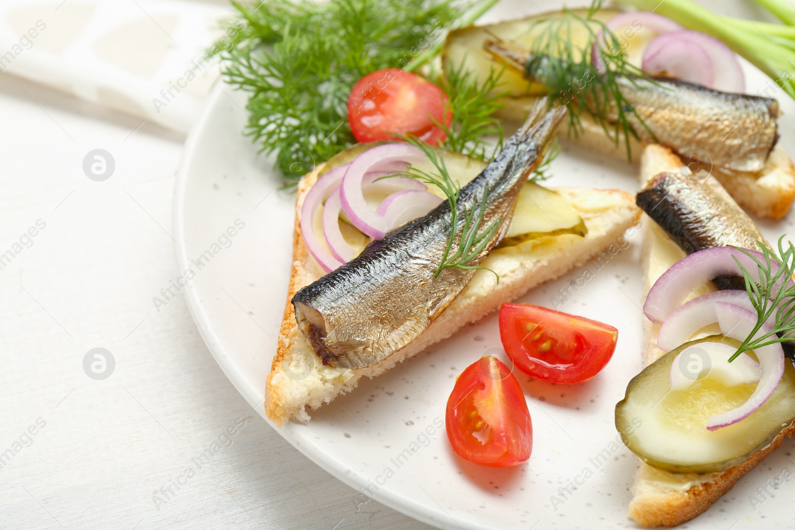 Delicious sandwiches with sprats, pickled cucumber, onion and dill served on white wooden table, closeup Photo of Delicious sandwiches with sprats, pickled cucumber, onion and dill served on white wooden table, closeup