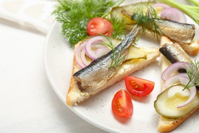Photo of Delicious sandwiches with sprats, pickled cucumber, onion and dill served on white wooden table, closeup