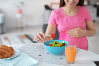 Photo of Young pregnant woman eating vegetable salad at table in kitchen