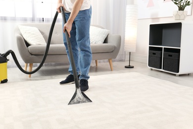 Man removing dirt from carpet with vacuum cleaner indoors, closeup