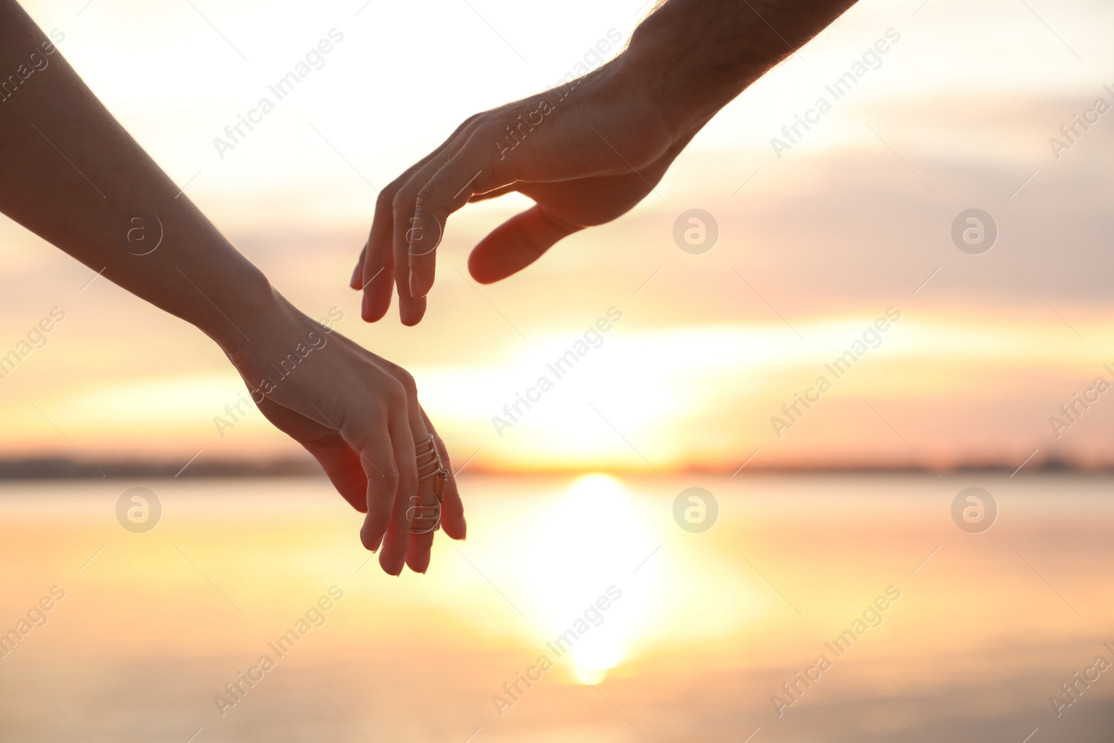 Photo of Man and woman reaching hands to each other at sunset, closeup. Nature healing power