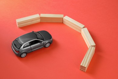 Development through barriers overcoming. Silver toy car movement blocked by wooden blocks on coral background