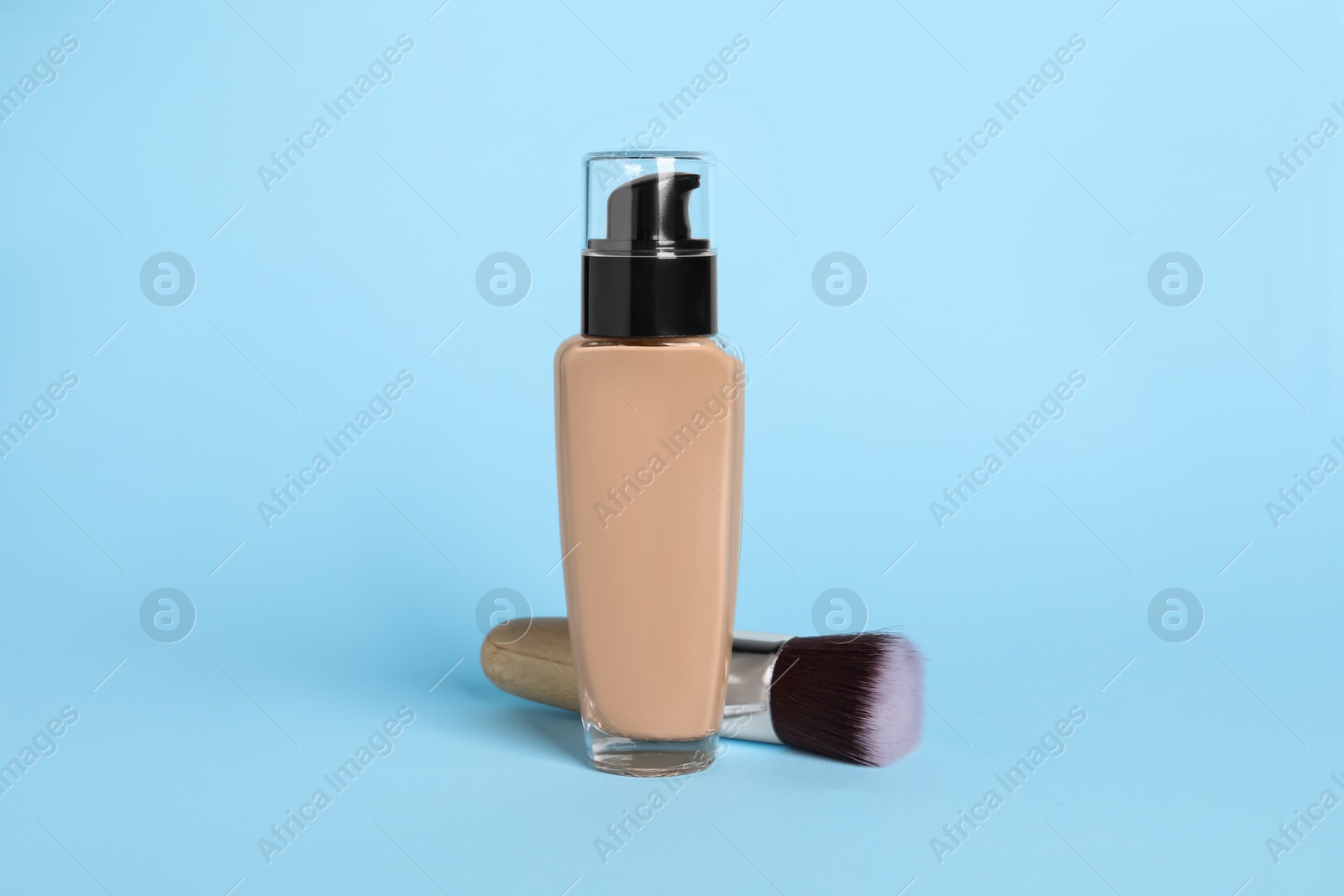 Photo of Bottle of skin foundation and brush on light blue background. Makeup product