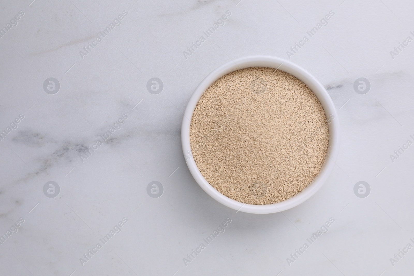 Photo of Bowl of active dry yeast on white marble table, top view. Space for text