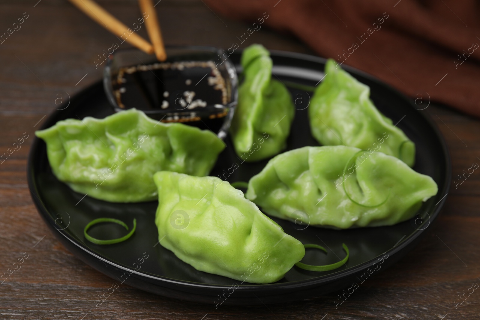 Photo of Delicious green dumplings (gyozas) and soy sauce on wooden table, closeup